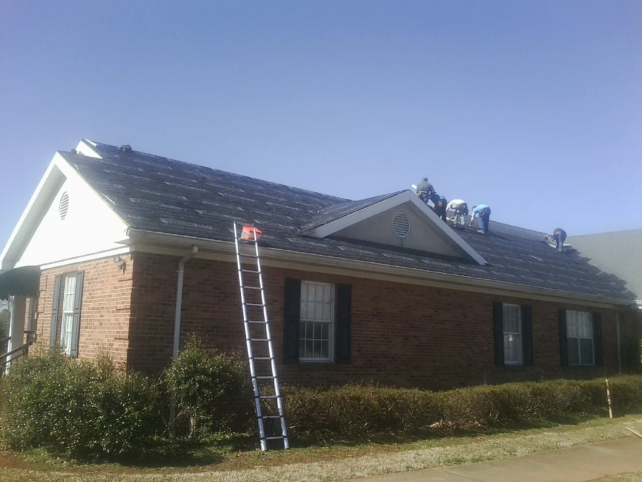 Crew tearing shingles off a brick ranch roof with a ladder set — Metal Roof Repair work by our crew in Amanda Park