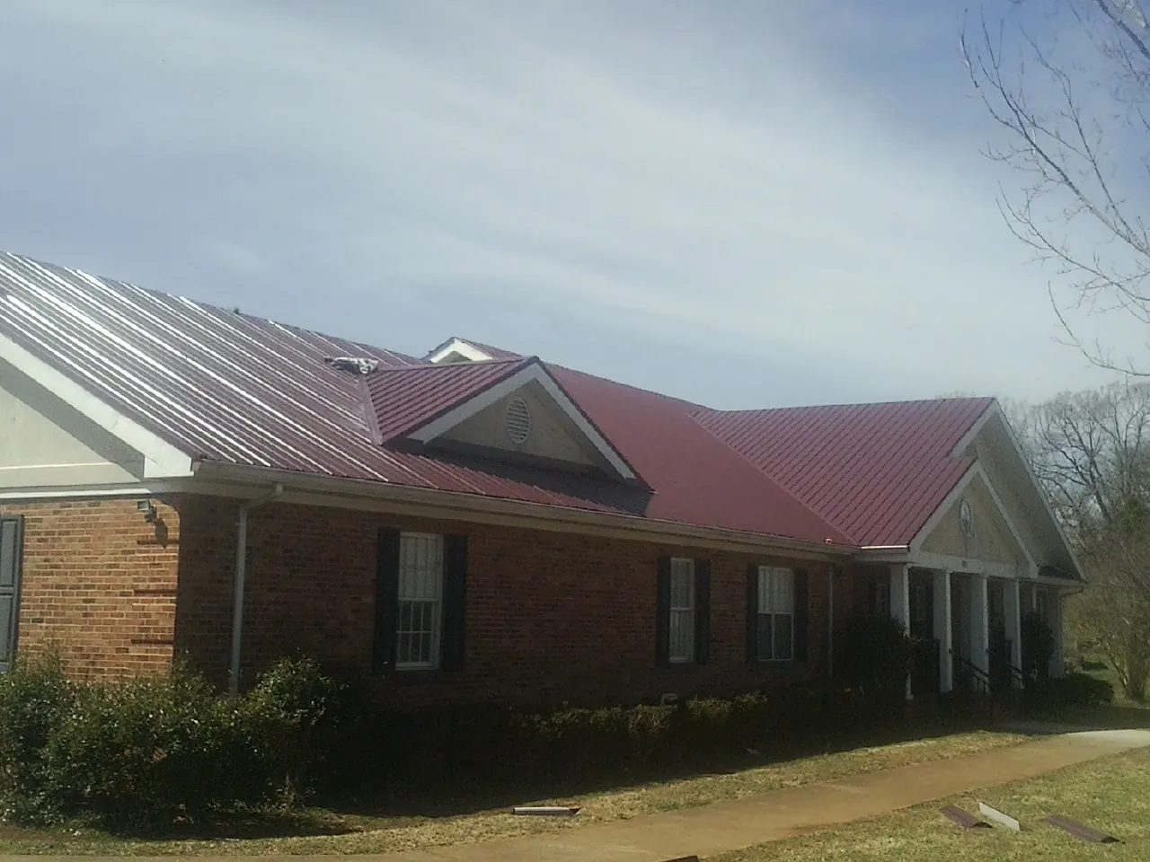 Red metal roof with gabled entries on a long brick building, from a Hail Damage Roof Repair job in Amanda Park