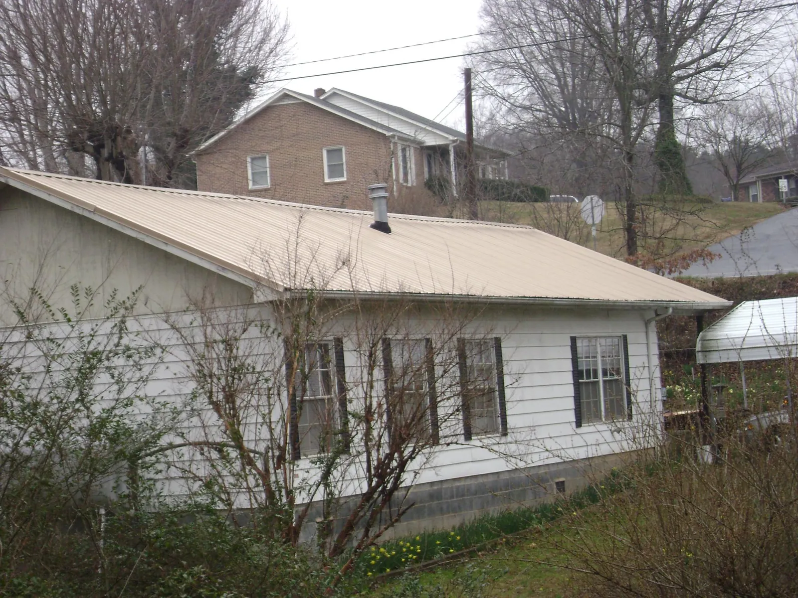 Tan metal roof on a white sided house set into a hillside in Amanda Park